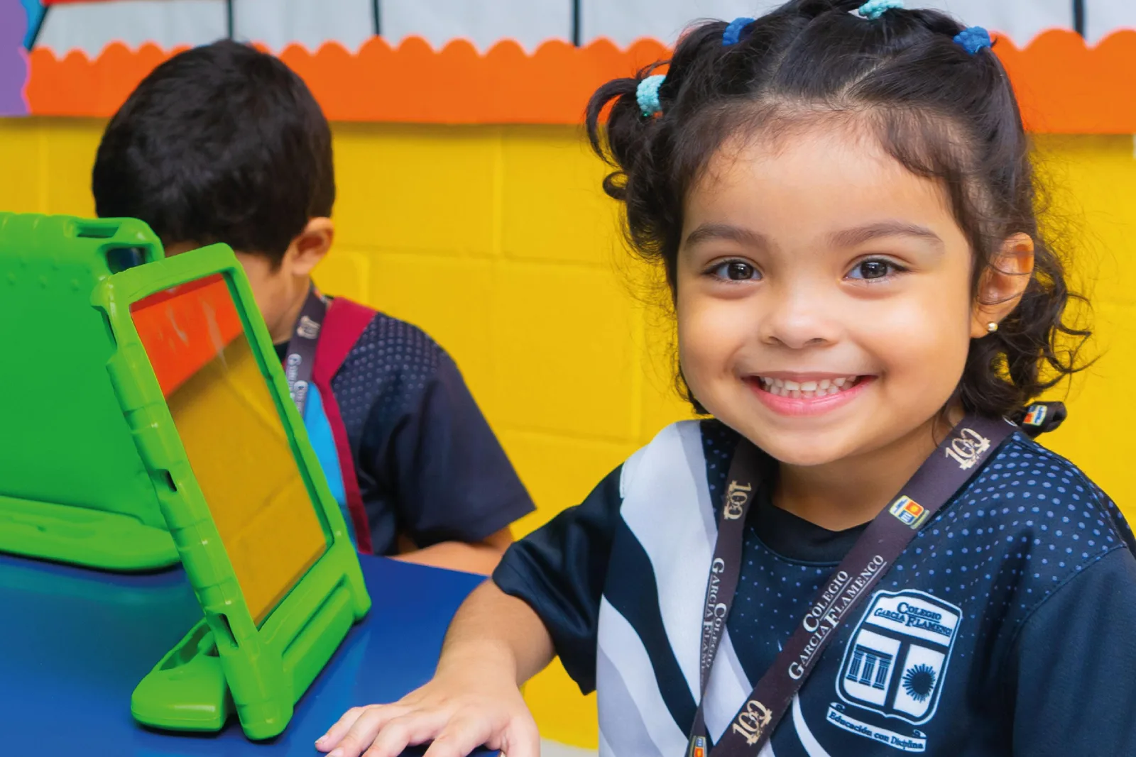 Niña de Parvularia sonriendo junto a una tableta en el aula